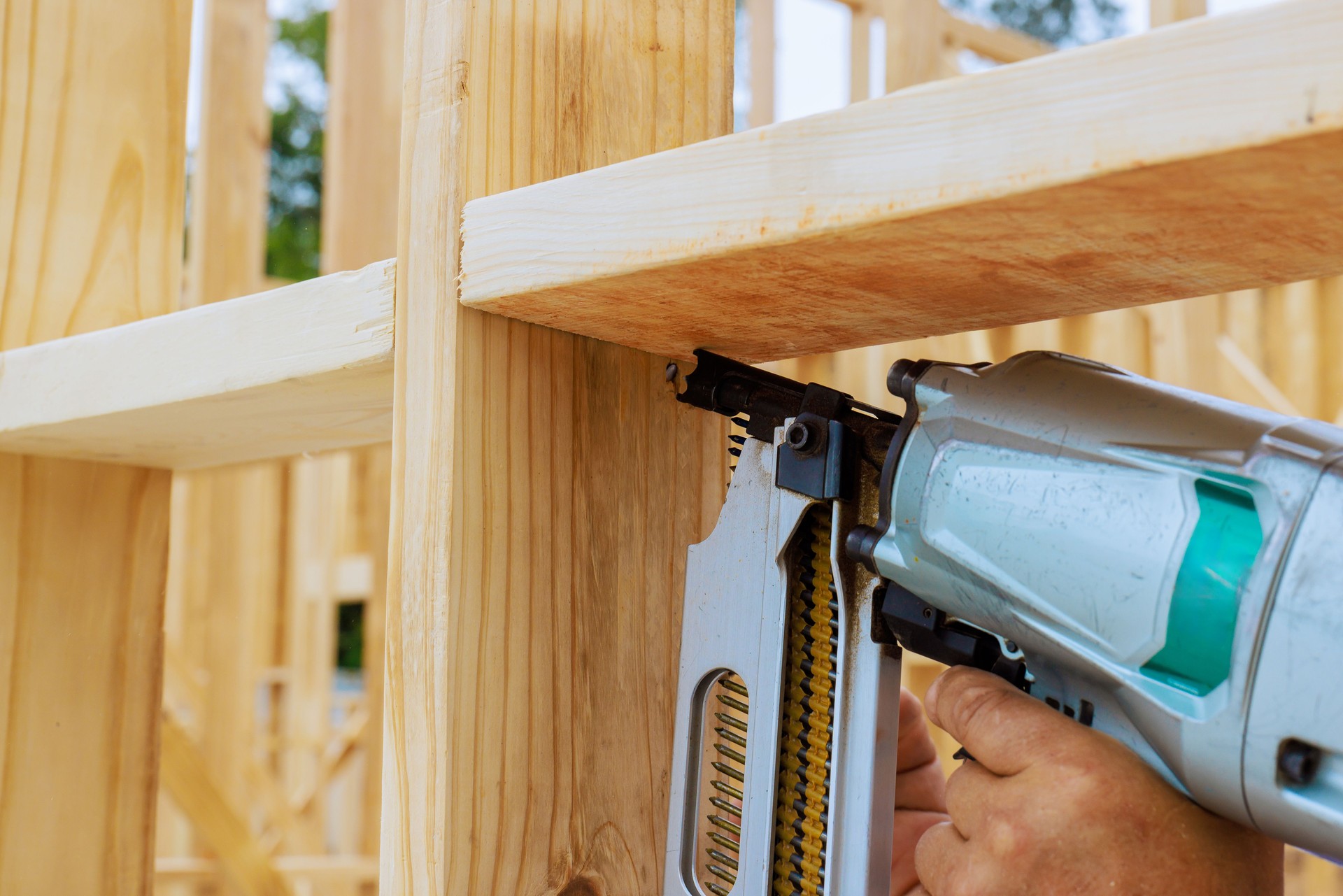 Construction worker using nail gun on wooden frame in bright daylight outdoors